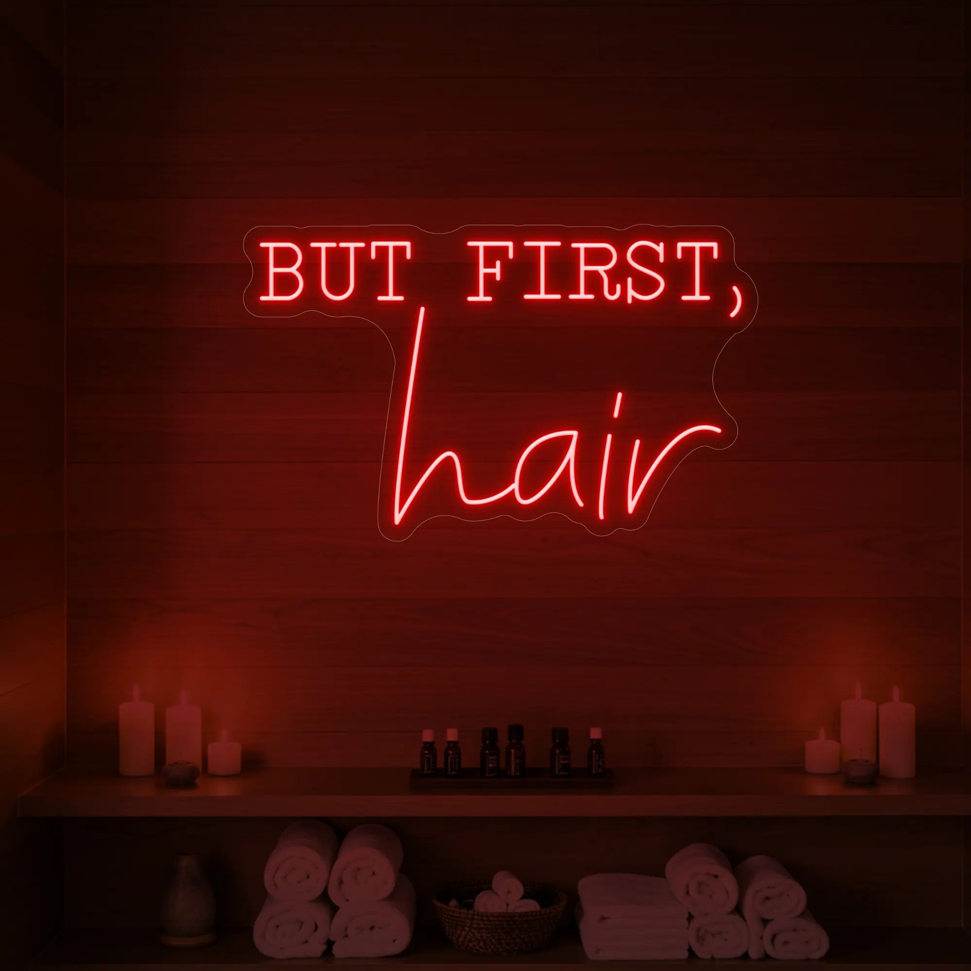Photo of the 'BUT FIRST, hair' neon sign glowing in red against a styled interior wall.