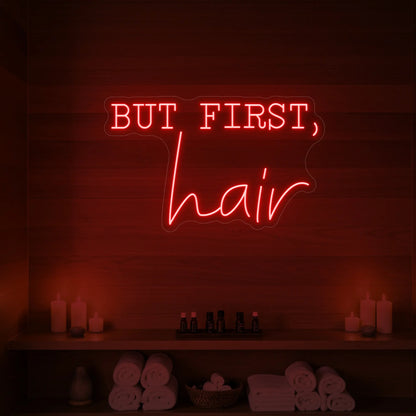 Photo of the 'BUT FIRST, hair' neon sign glowing in red against a styled interior wall.