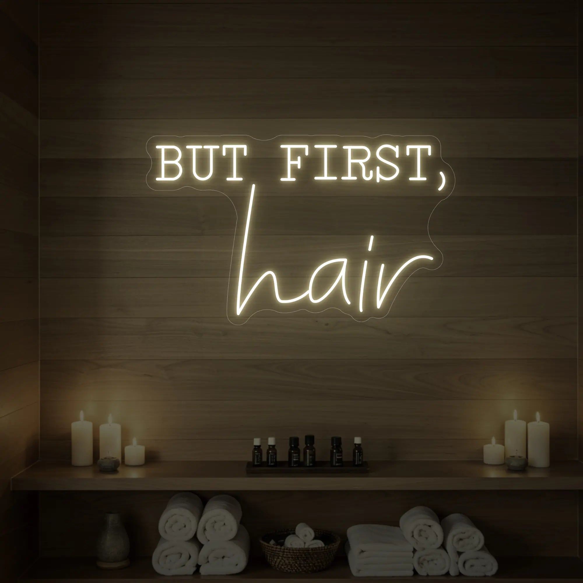 Photo of the 'BUT FIRST, hair' neon sign glowing in warm white against a styled interior wall.