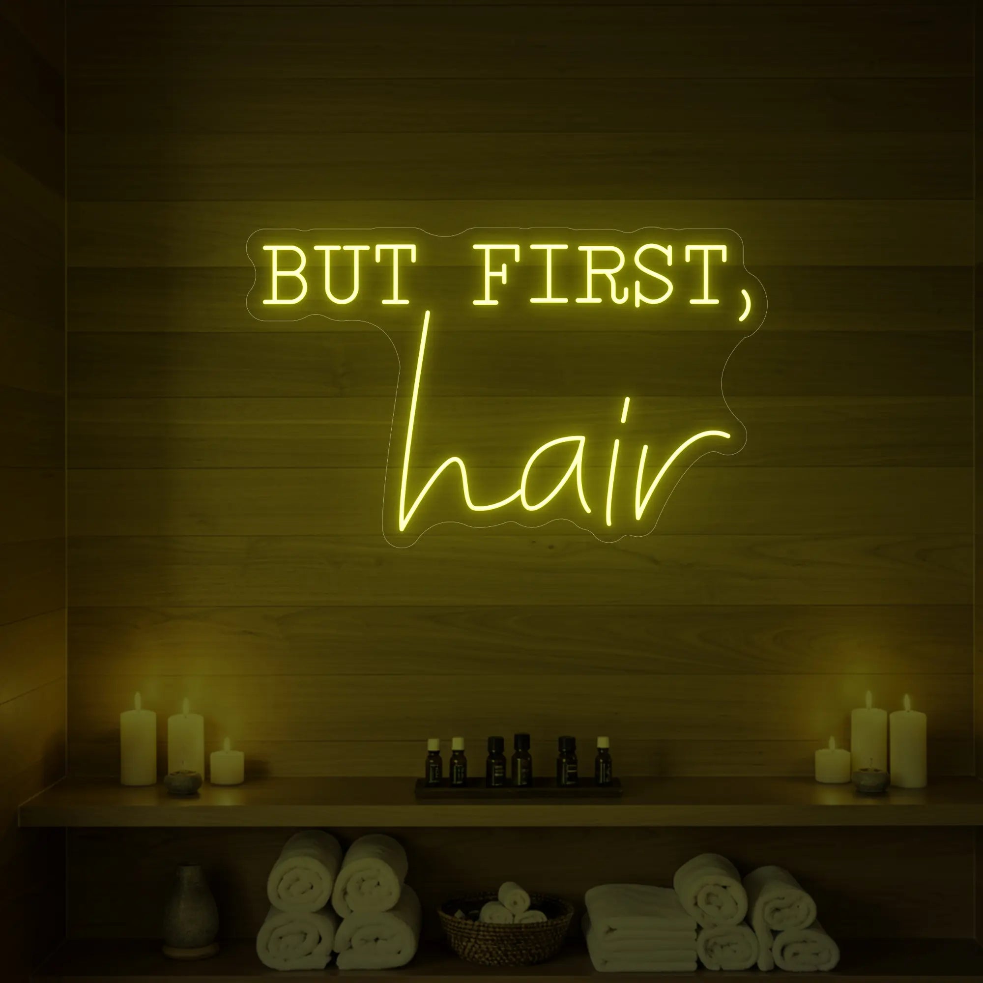 Photo of the 'BUT FIRST, hair' neon sign glowing in lemon yellow against a styled interior wall.