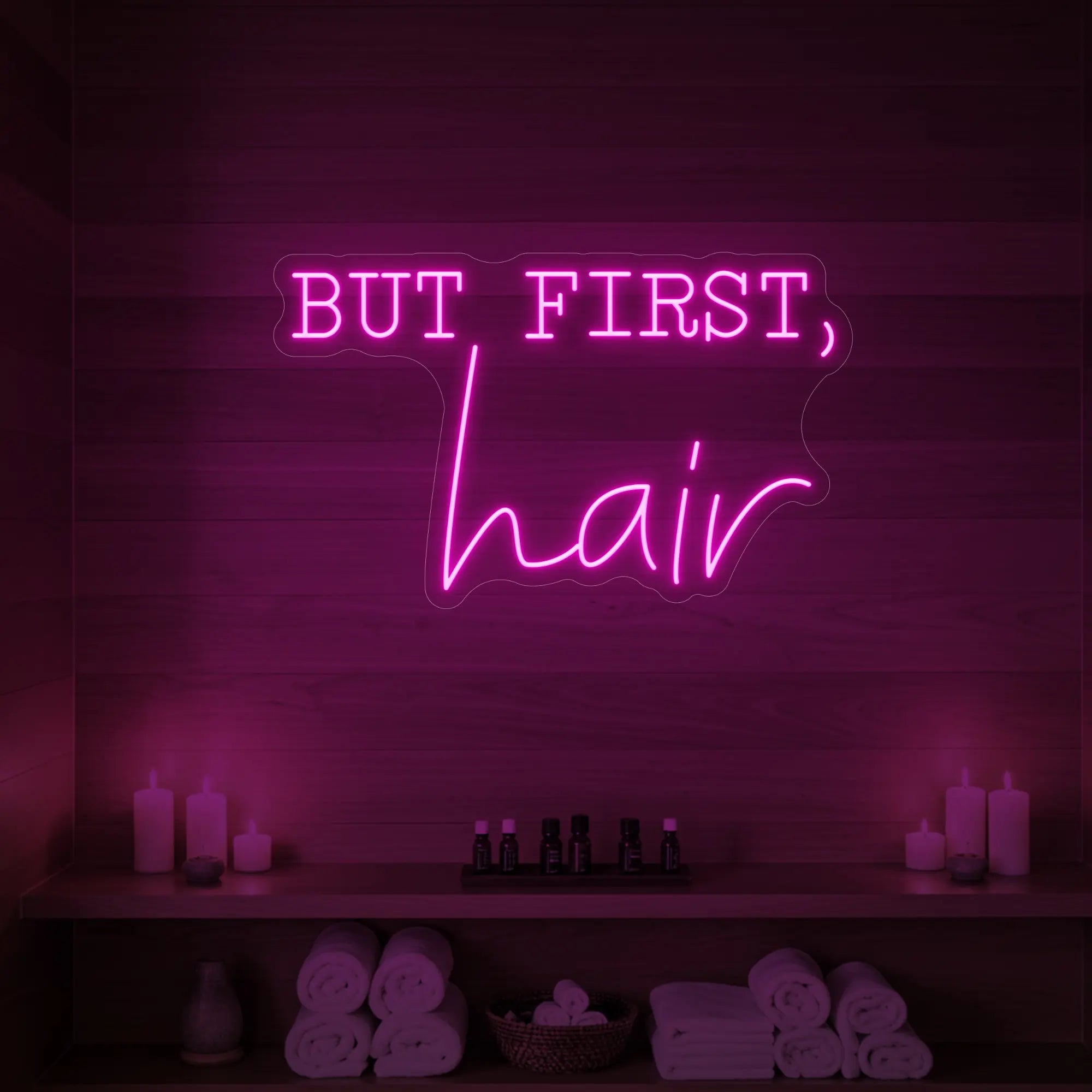 Photo of the 'BUT FIRST, hair' neon sign glowing in light pink against a styled interior wall.