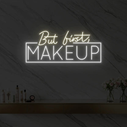 Photo of the 'But first, MAKEUP' neon sign glowing in warm white against a styled interior wall.