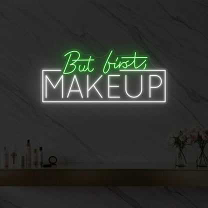 Photo of the 'But first, MAKEUP' neon sign glowing in green against a styled interior wall.