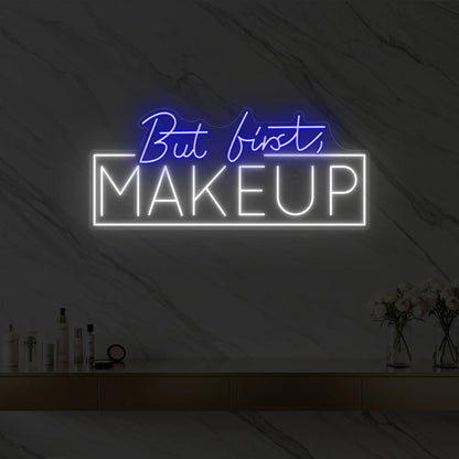 Photo of the 'But first, MAKEUP' neon sign glowing in deep blue against a styled interior wall.