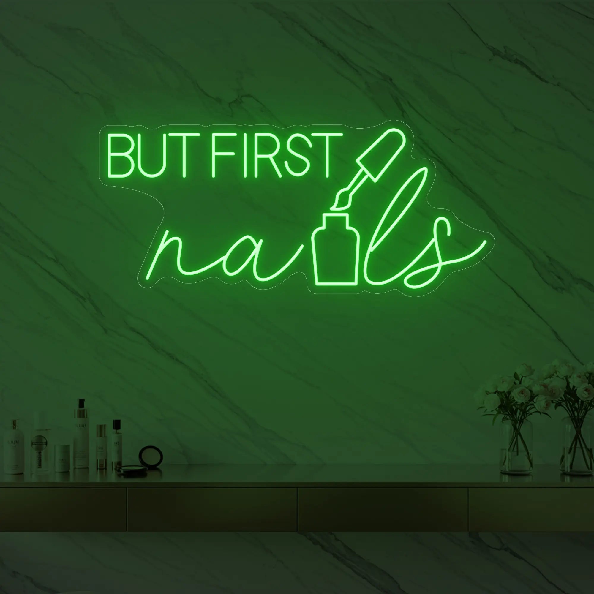 Photo of the 'BUT FIRST nails' neon sign with a nail polish bottle graphic glowing in green against a styled interior wall.