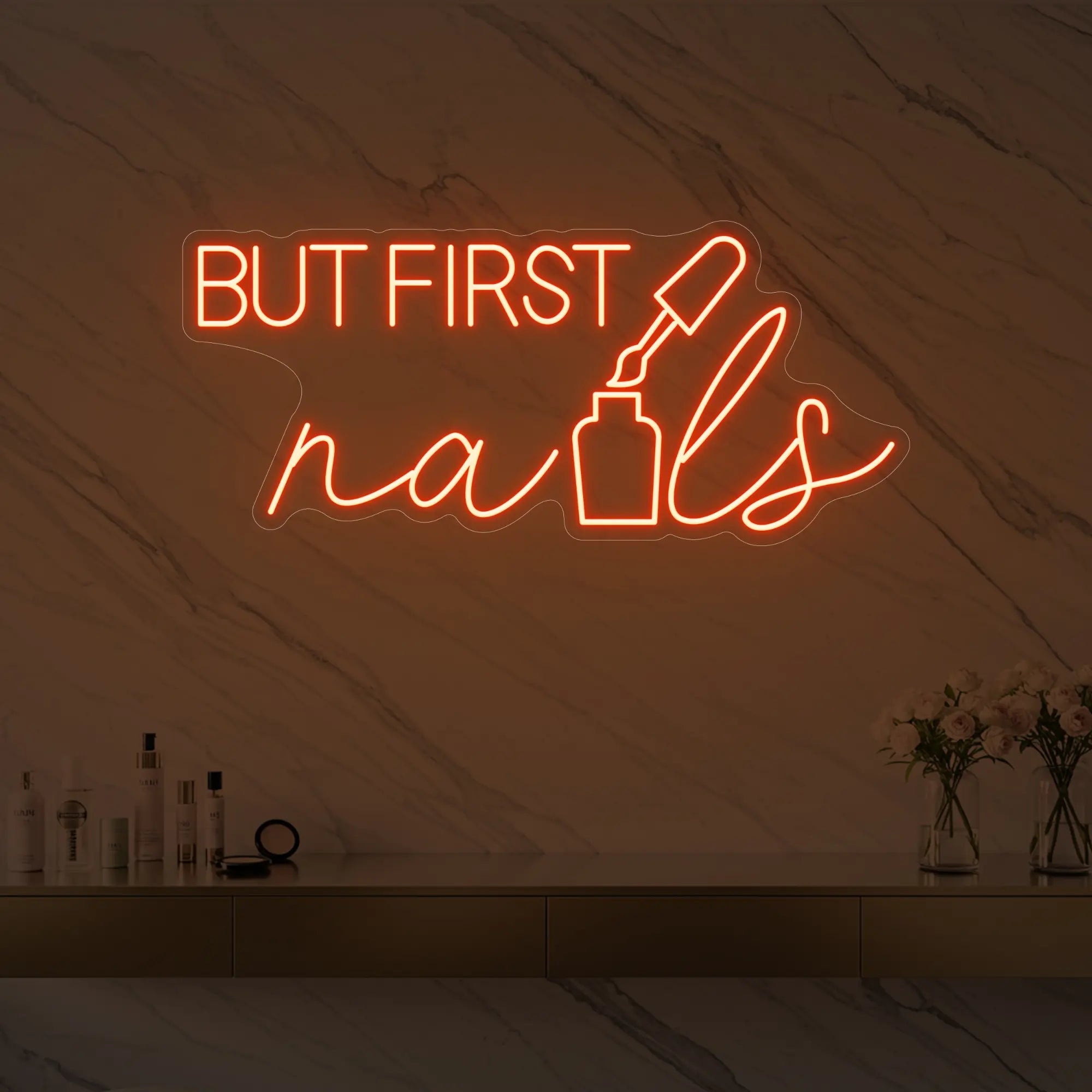 Photo of the 'BUT FIRST nails' neon sign with a nail polish bottle graphic glowing in golden yellow against a styled interior wall.