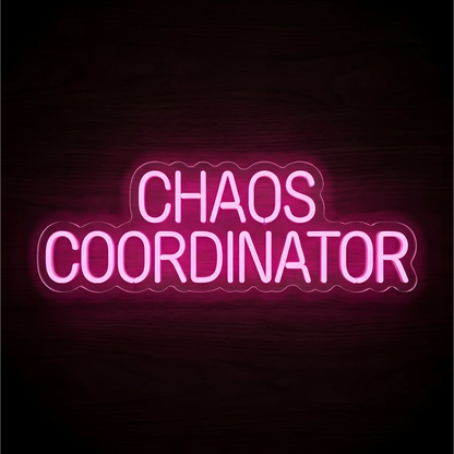 “CHAOS COORDINATOR” LED Neon Sign glowing in bright pink uppercase lettering across two lines on clear acrylic against a dark wood background, suited to home offices and team workspaces.