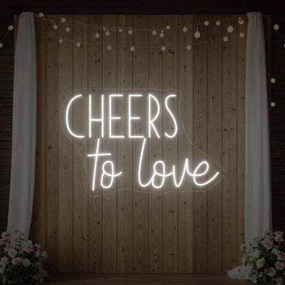 Photo of the 'Cheers To Love' neon sign glowing in cool white against a styled interior wall.