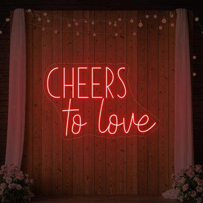 Photo of the 'Cheers To Love' neon sign glowing in red against a styled interior wall.