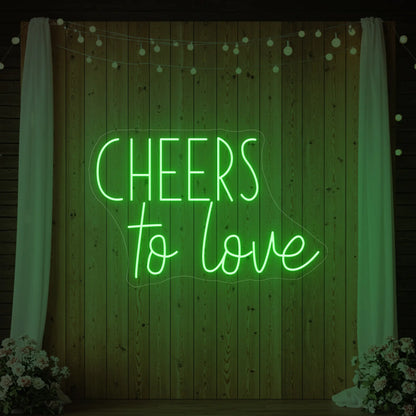 Photo of the 'Cheers To Love' neon sign glowing in green against a styled interior wall.