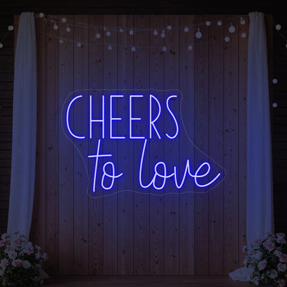 Photo of the 'Cheers To Love' neon sign glowing in deep blue against a styled interior wall.