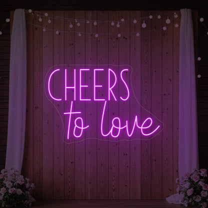 Photo of the 'Cheers To Love' neon sign glowing in deep pink against a styled interior wall.