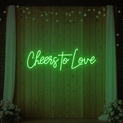 Photo of the 'Cheers To Love' neon sign glowing in green against a styled interior wall.