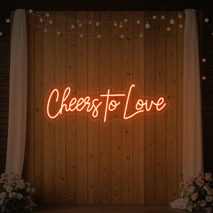 Photo of the 'Cheers To Love' neon sign glowing in golden yellow against a styled interior wall.