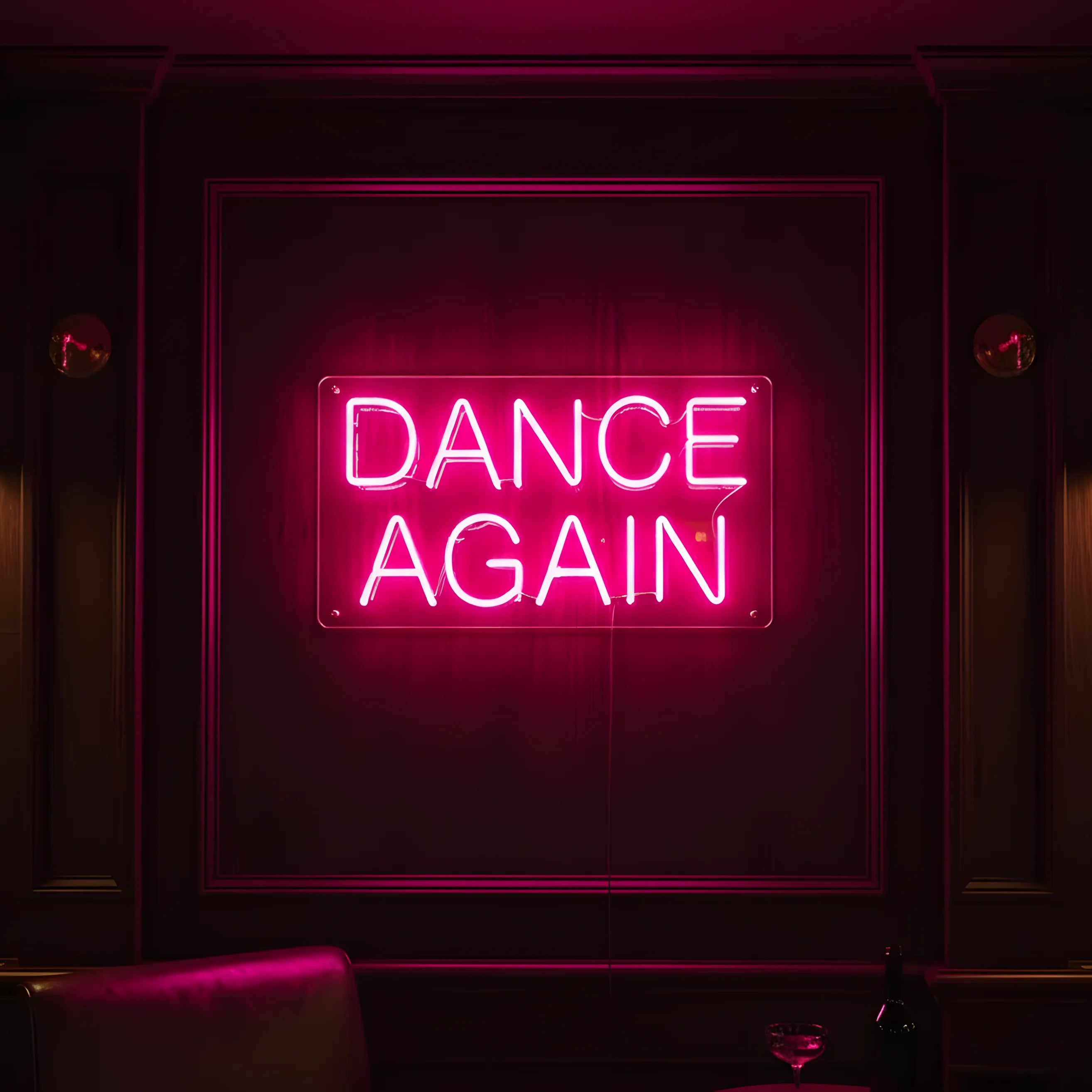 Photo of the 'DANCE AGAIN' neon sign glowing in pink against a modern nightclub-inspired wall.