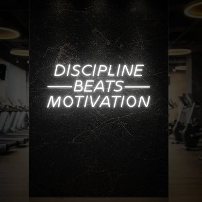 'Discipline Beats Motivation' neon sign glowing in cool white against a styled interior wall.