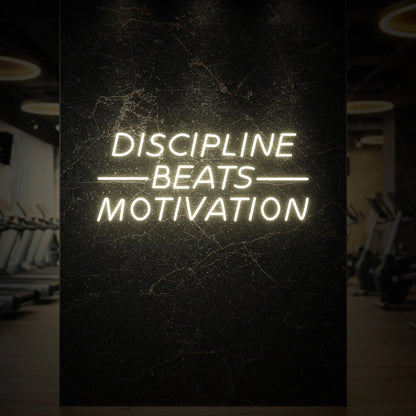 'Discipline Beats Motivation' neon sign glowing in warm white against a styled interior wall.