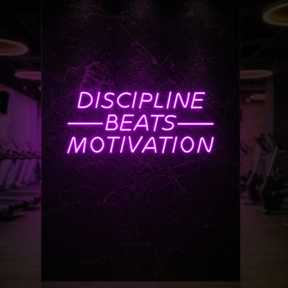 'Discipline Beats Motivation' neon sign glowing in deep pink against a styled interior wall.