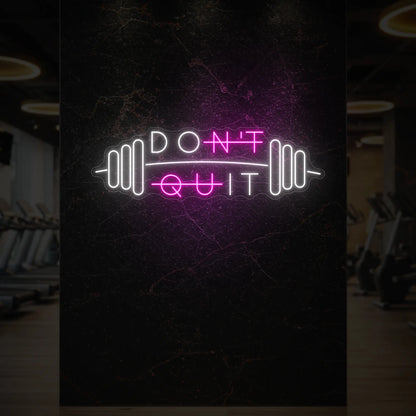  'Don’t Quit (with Barbell)' neon sign glowing in light pink against a styled interior wall.