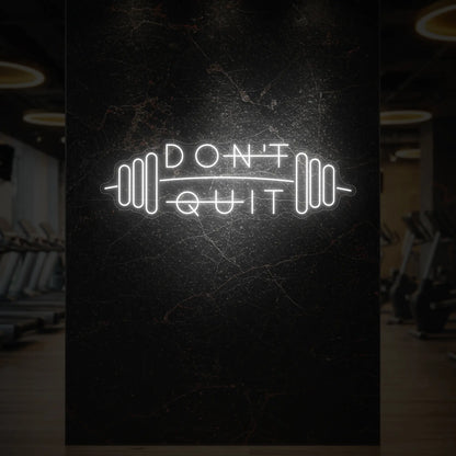  'Don’t Quit (with Barbell)' neon sign glowing in cool white against a styled interior wall.