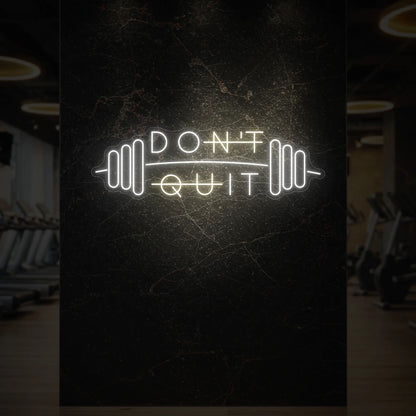 'Don’t Quit (with Barbell)' neon sign glowing in warm white against a styled interior wall.