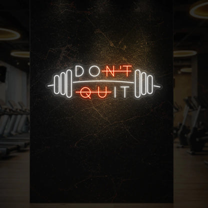 'Don’t Quit (with Barbell)' neon sign glowing in golden yellow against a styled interior wall.