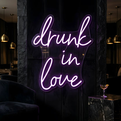 Photo of the 'Drunk in Love' neon sign glowing in purple against a styled interior wall.