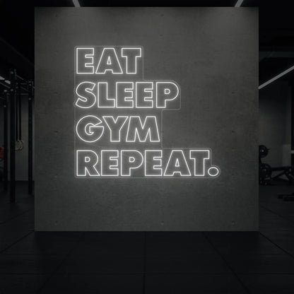  'Eat Sleep Gym Repeat' neon sign glowing in cool white against a styled interior wall.
