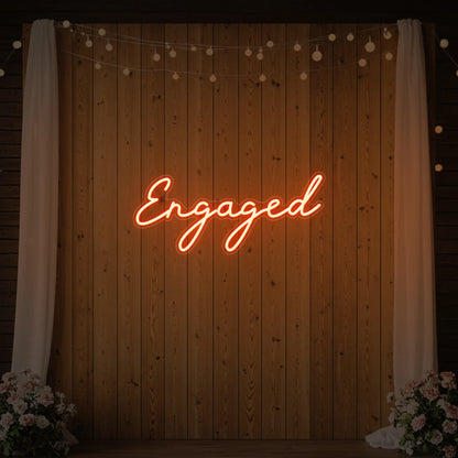 Photo of the 'Engaged' neon sign glowing in golden yellow against a styled interior wall.