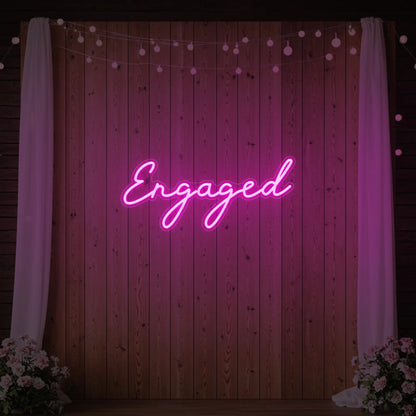 Photo of the 'Engaged' neon sign glowing in light pink against a styled interior wall.