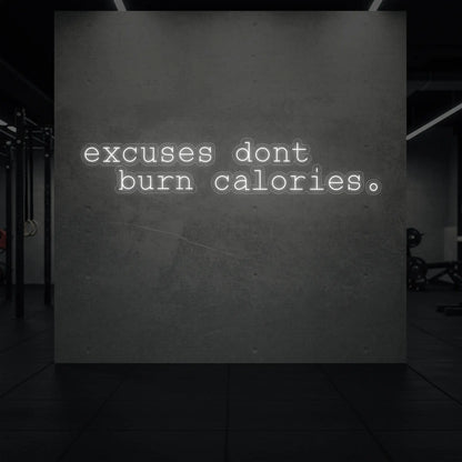 'Excuses Don’t Burn Calories' neon sign glowing in cool white against a styled interior wall.