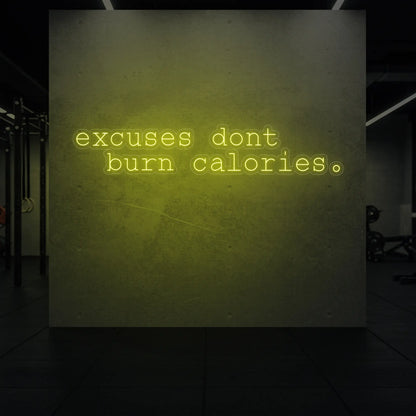  'Excuses Don’t Burn Calories' neon sign glowing in lemon yellow against a styled interior wall.
