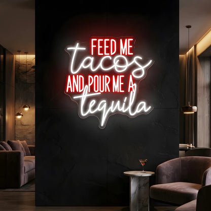 Photo of the 'Feed Me Tacos and Pour Me a Tequila' neon sign glowing in multi-color against a styled interior wall.