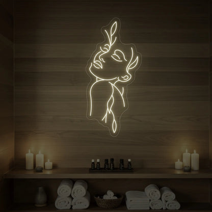 Photo of the 'Flower Girl' neon sign featuring a minimalist face and leaf line art glowing in warm white against a styled interior wall.