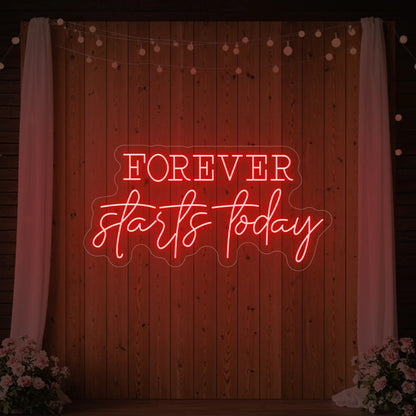 Photo of the 'Forever Starts Today' neon sign glowing in red against a styled interior wall.