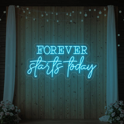 Photo of the 'Forever Starts Today' neon sign glowing in ice blue against a styled interior wall.