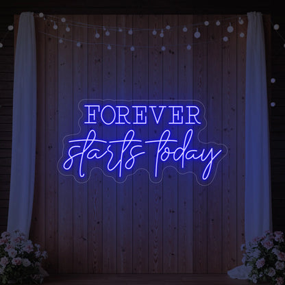 Photo of the 'Forever Starts Today' neon sign glowing in deep blue against a styled interior wall.