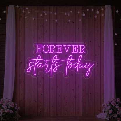 Photo of the 'Forever Starts Today' neon sign glowing in deep pink against a styled interior wall.