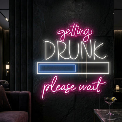 Photo of the 'Getting Drunk Please Wait' neon sign glowing in multi-color against a styled interior wall.