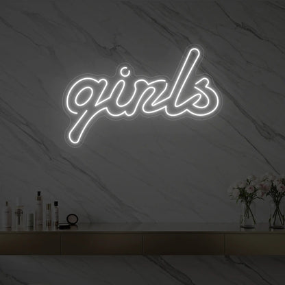Photo of the 'girls' neon sign in playful script glowing in cool white against a styled interior wall.