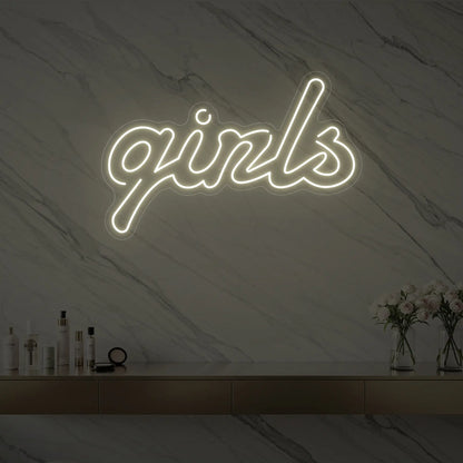 Photo of the 'girls' neon sign in playful script glowing in warm white against a styled interior wall.
