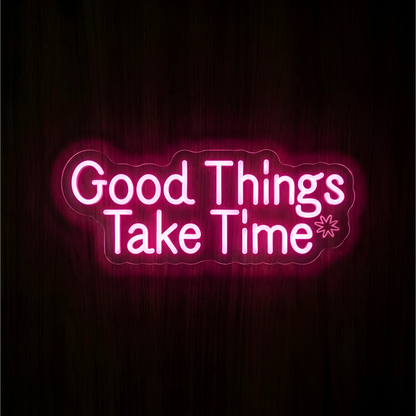 “Good Things Take Time” LED Neon Sign glowing in pink lettering with a small outlined starburst on clear acrylic against a dark wood background, suited to bedrooms and home offices.