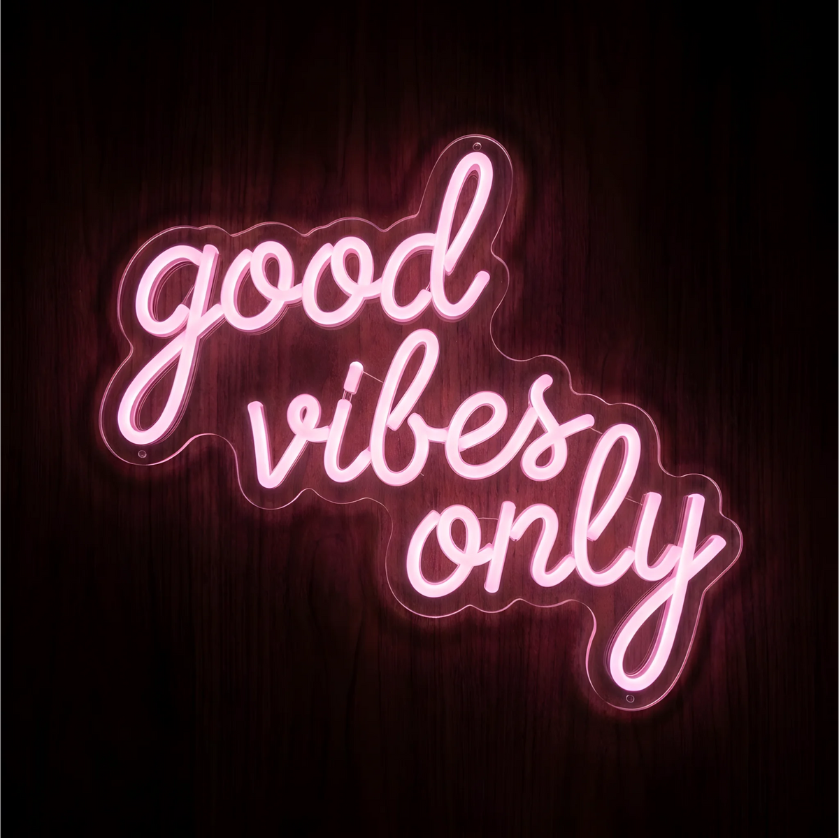 Good Vibes Only LED Neon Sign featuring glowing pink cursive lettering on contoured clear acrylic backing against a dark wood background, ideal for bedrooms, salons, and positive quote wall decor.