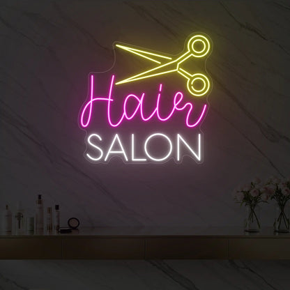 Photo of the 'Hair Salon' neon sign with a scissors icon glowing in cool white, pink, and lemon yellow against a styled interior wall.