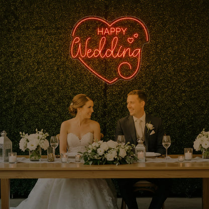 Photo of the 'Happy Wedding' neon sign glowing in golden yellow against a styled interior wall.