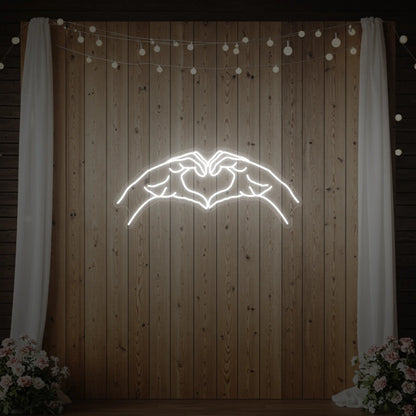Photo of the 'Heart Hands' neon sign glowing in cool white against a styled interior wall.