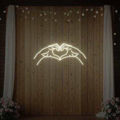 Photo of the 'Heart Hands' neon sign glowing in warm white against a styled interior wall.