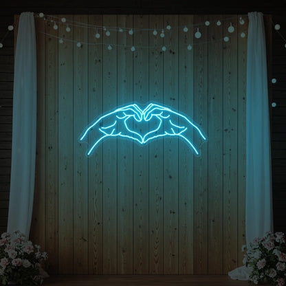 Photo of the 'Heart Hands' neon sign glowing in ice blue against a styled interior wall.