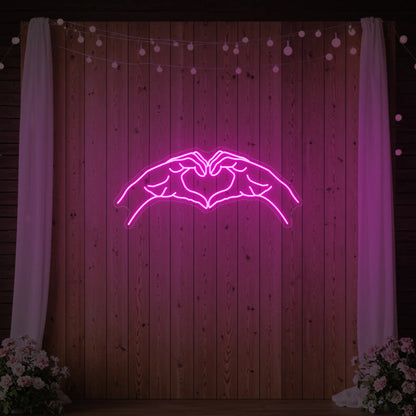 Photo of the 'Heart Hands' neon sign glowing in light pink against a styled interior wall.