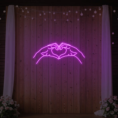 Photo of the 'Heart Hands' neon sign glowing in deep pink against a styled interior wall.